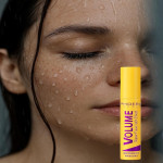 Close-up of a woman's face with water droplets, holding a yellow tube labeled Phoera Volume Waterproof Mascara beside her cheek.